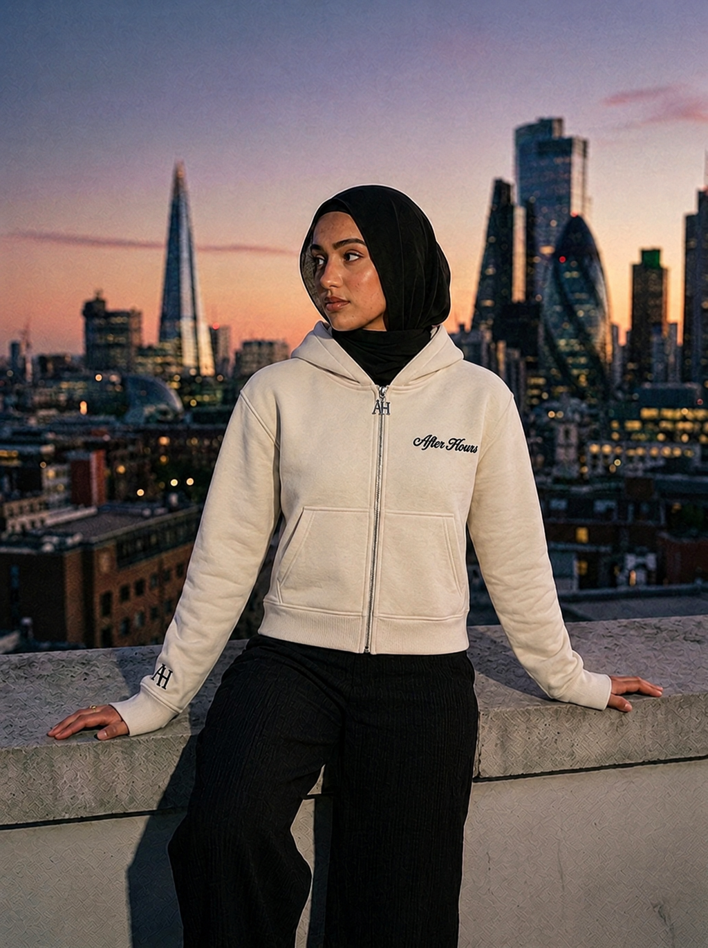 Model in a hijab wearing the fitted cream After Hours Signature Zip Hoodie on a London rooftop